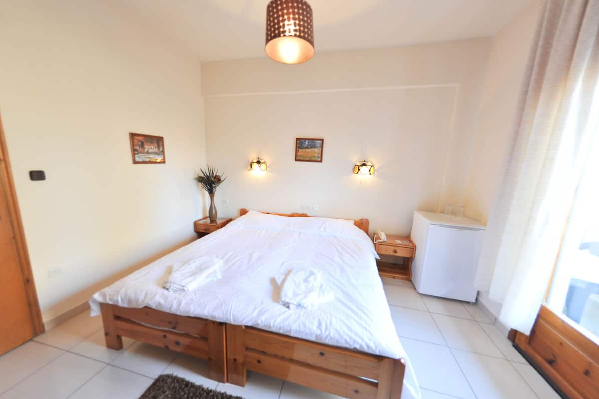 A bedroom with a wooden bed, bedside tables, a small white cabinet, wall-mounted lights, and a ceiling light fixture.