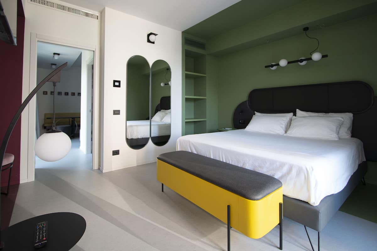 A modern bedroom with a large bed, a bench, and a mirror.