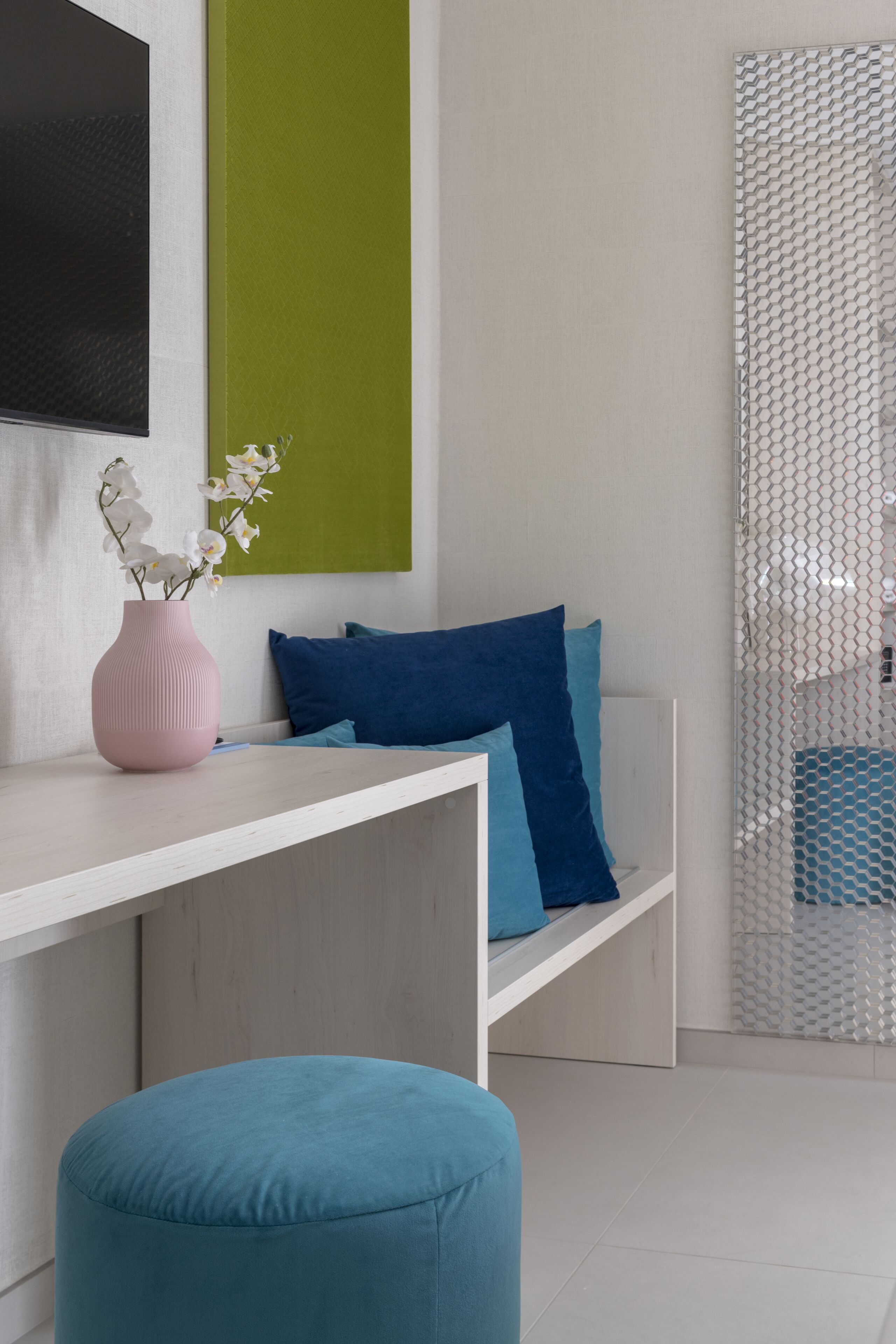 A modern room with a white sofa, blue cushions, a pink vase with white flowers, and a teal ottoman.