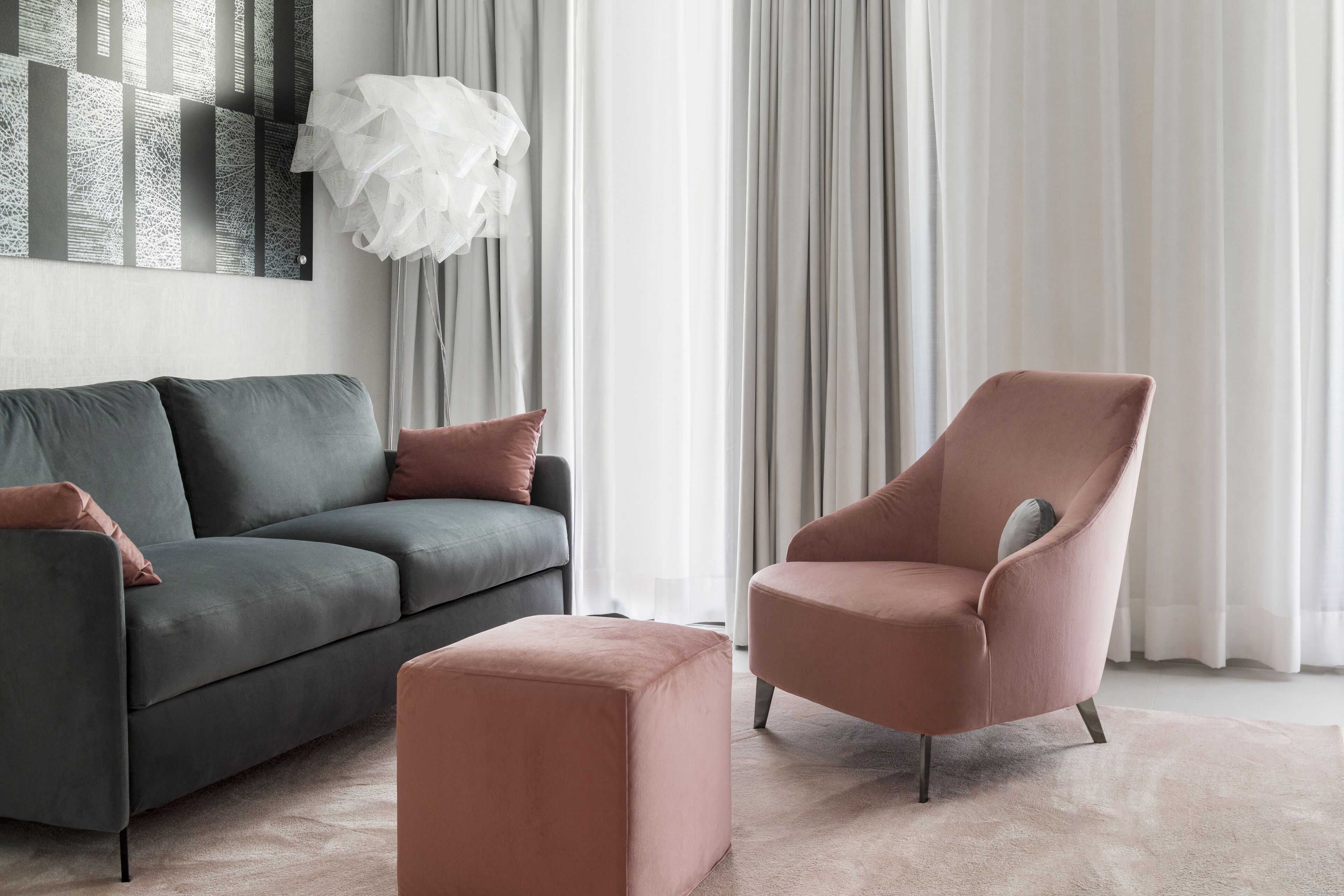 Een moderne woonkamer met een grijze bank, een roze fauteuil en een bijpassend poef.