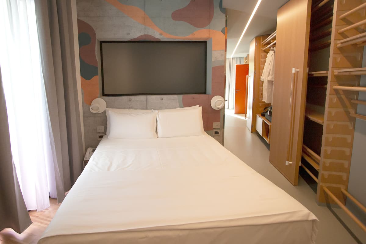 A hotel room with a large bed, a wardrobe, and a television mounted on the wall.