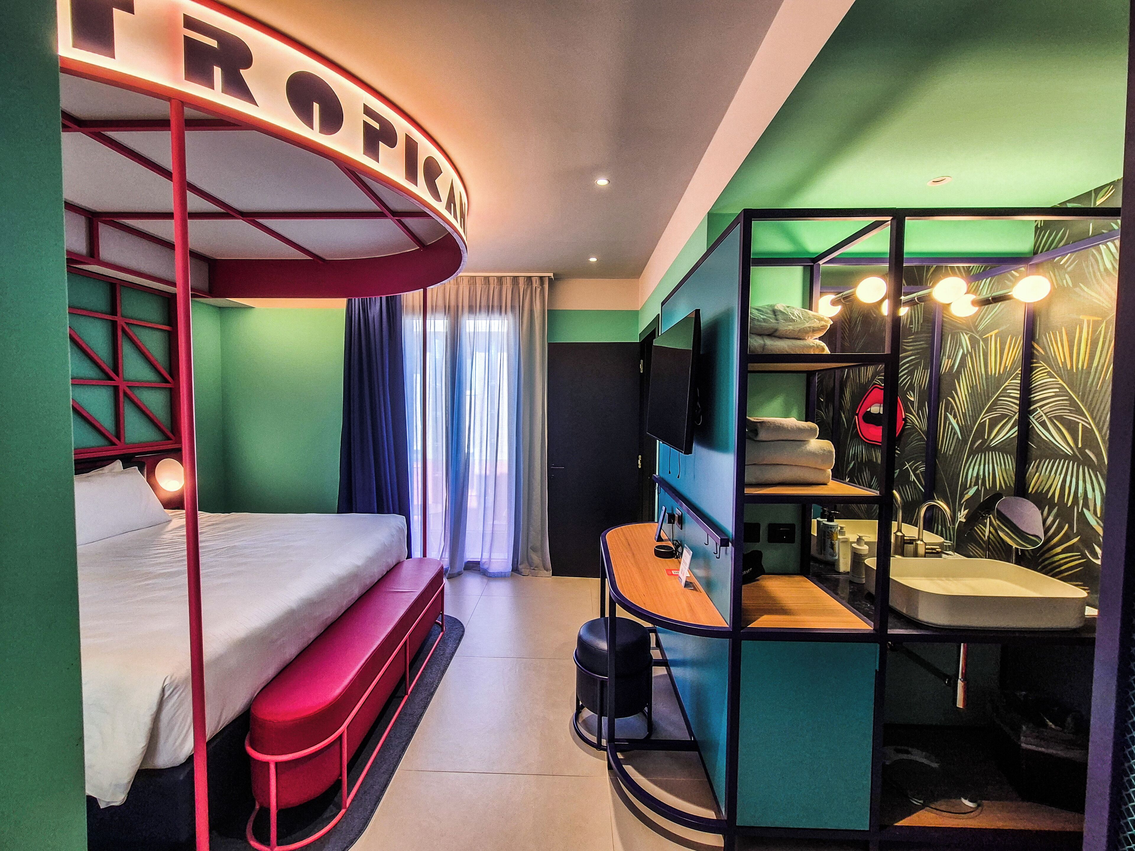 A room with bunk beds, a desk, a TV, and a bathroom with a mirror and sink.