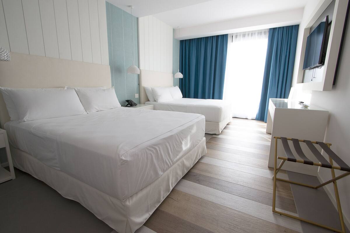 A hotel room with a large bed, a smaller bed, a desk, and a chair.