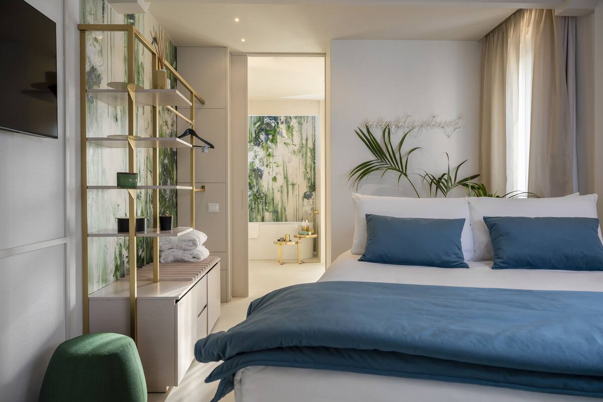 A modern bedroom with a large bed, a built-in wardrobe, a desk, and a green chair.