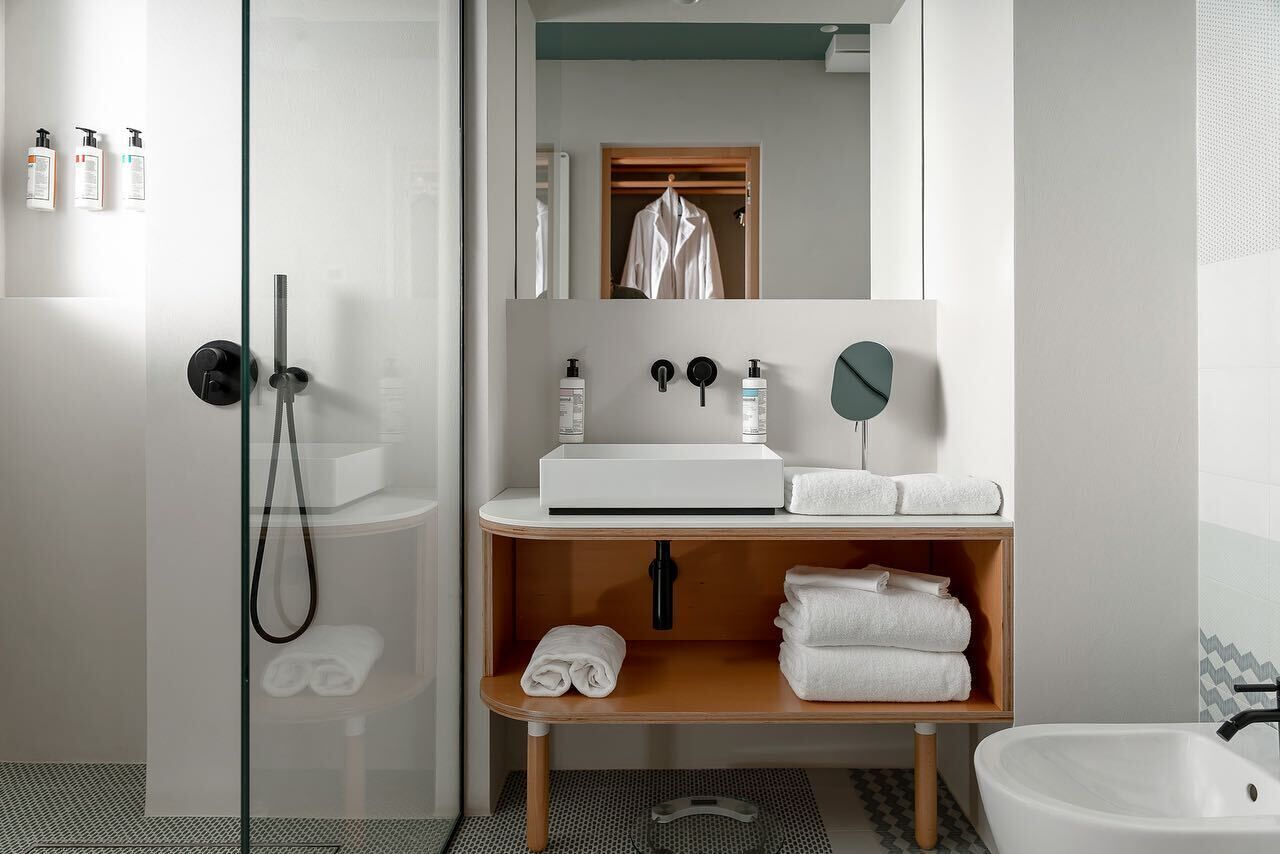 Un baño moderno con ducha de vidrio, un lavamanos blanco y un mueble de tocador de madera con toallas.