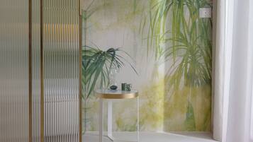 Habitación con un mural de plantas tropicales, una pequeña mesa con un florero y un biombo decorativo.