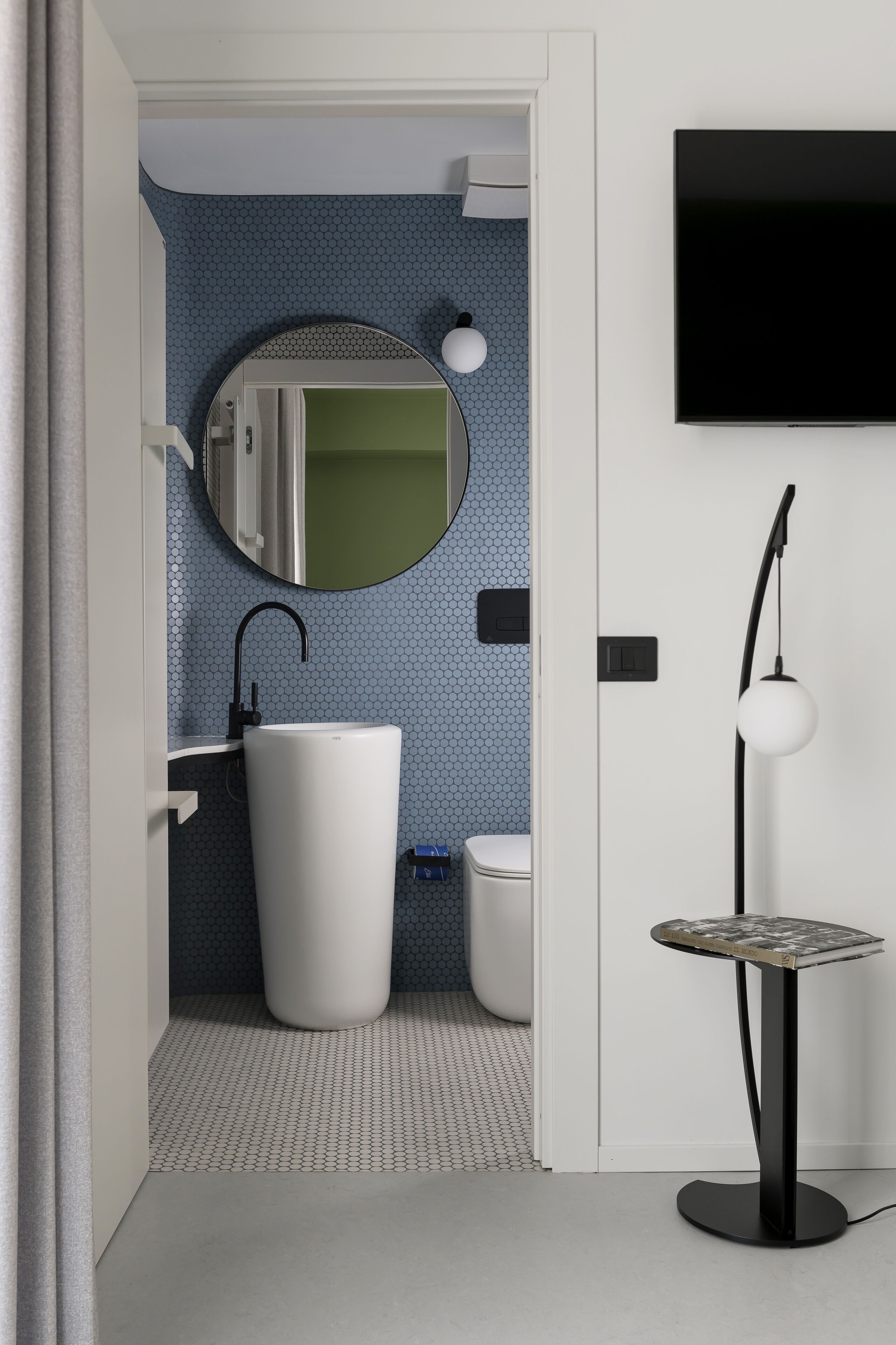 A modern bathroom with a white sink, a round mirror, and a toilet.
