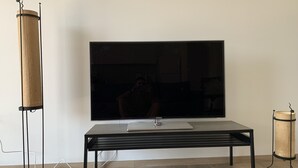 Una sala de estar moderna con un televisor de pantalla plana montado en la pared, una mesa de centro de madera y una lámpara de pie alta.