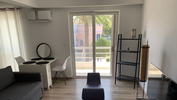 Una sala de estar moderna con un sofá, un escritorio, una silla y un ventanal con vistas a edificios y zonas verdes.