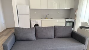 Un sofá gris con tres cojines en una cocina moderna con armarios blancos, una lavadora y una estufa.