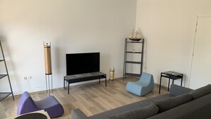 Una sala de estar moderna con un televisor de pantalla plana, un sillón azul, un sofá gris y una mesita.