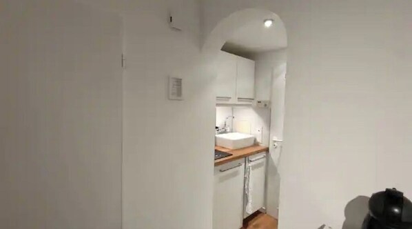 A narrow hallway leading to a kitchen with white cabinets, a wooden countertop, and a sink.