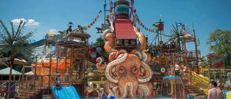 A water park with a large octopus-themed play structure, slides, and a sandy play area.