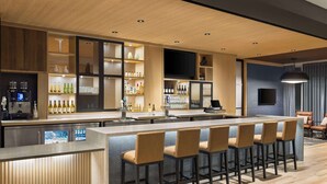 Un área de bar moderna con una barra larga, taburetes y estantes llenos de botellas y vasos.