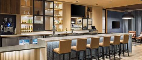 Un área de bar moderna con una barra larga, taburetes y estantes llenos de botellas y vasos.