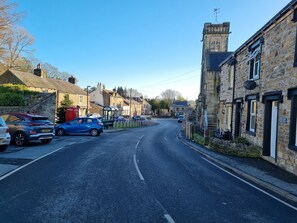 A street lined with stone buildings, parked cars, and a clear blue sky.