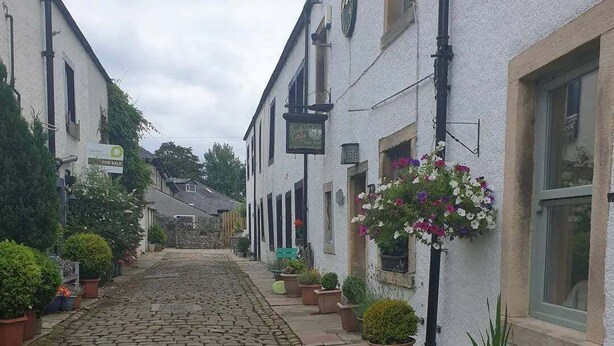 A cobblestone street lined with white buildings, some with flower baskets and potted plants. - Bashall Barn, Eaves Hall, Outbarn all Close by (Clitheroe)