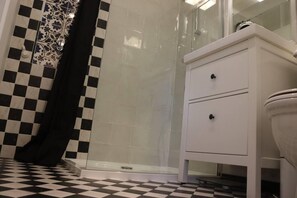 A bathroom with a checkered floor, a white vanity with two drawers, and a glass shower enclosure.