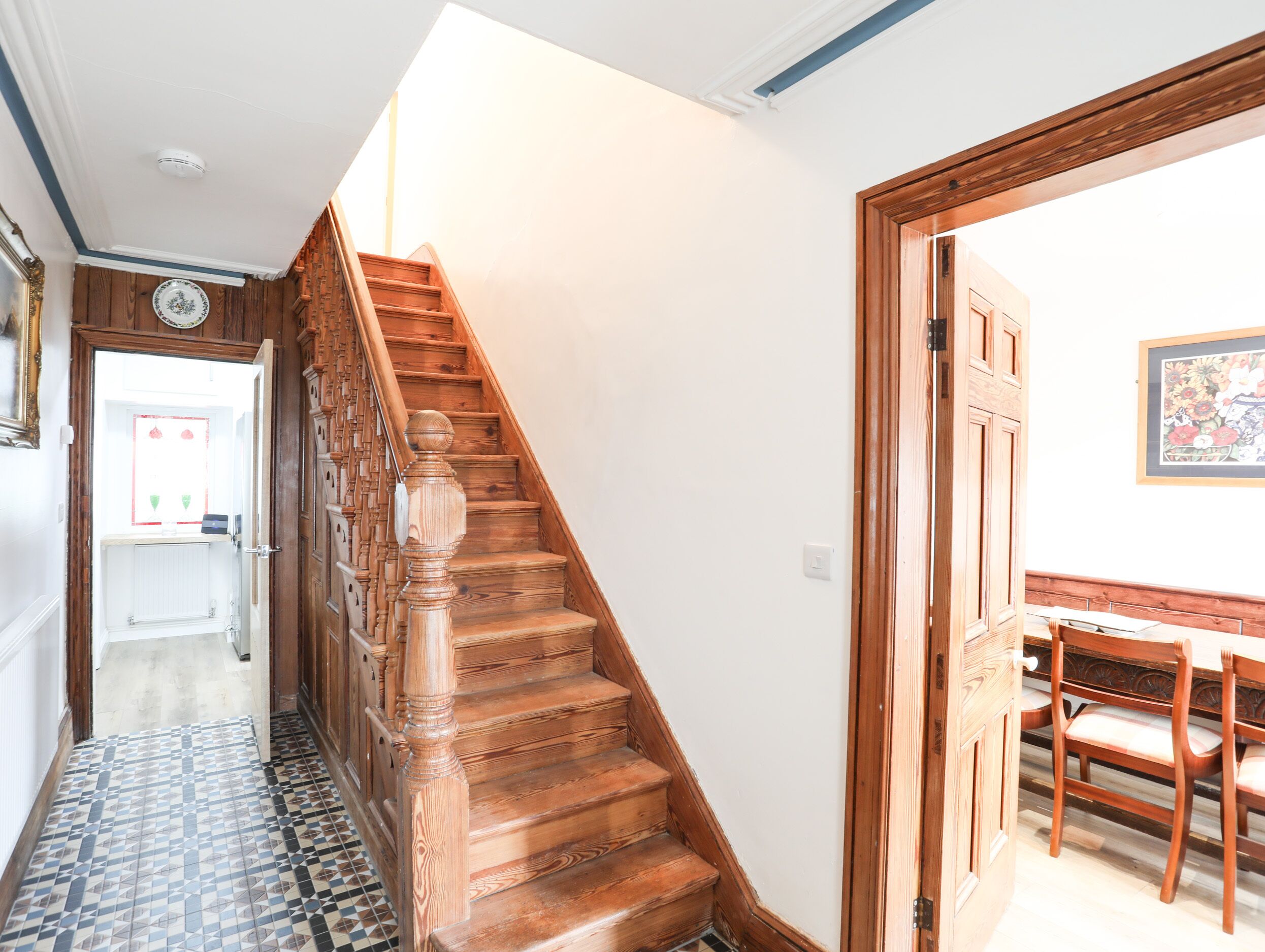 A wooden staircase with a handrail, leading to a room with a dining table and chairs.