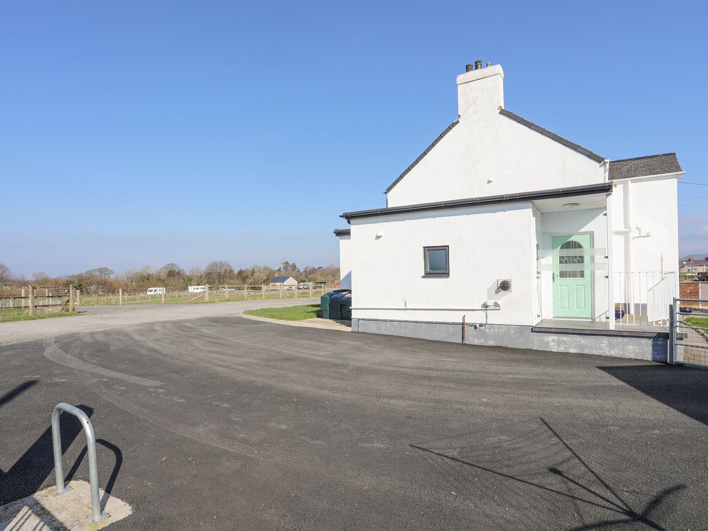 A white building with a green door, a small window, and a fenced driveway.
