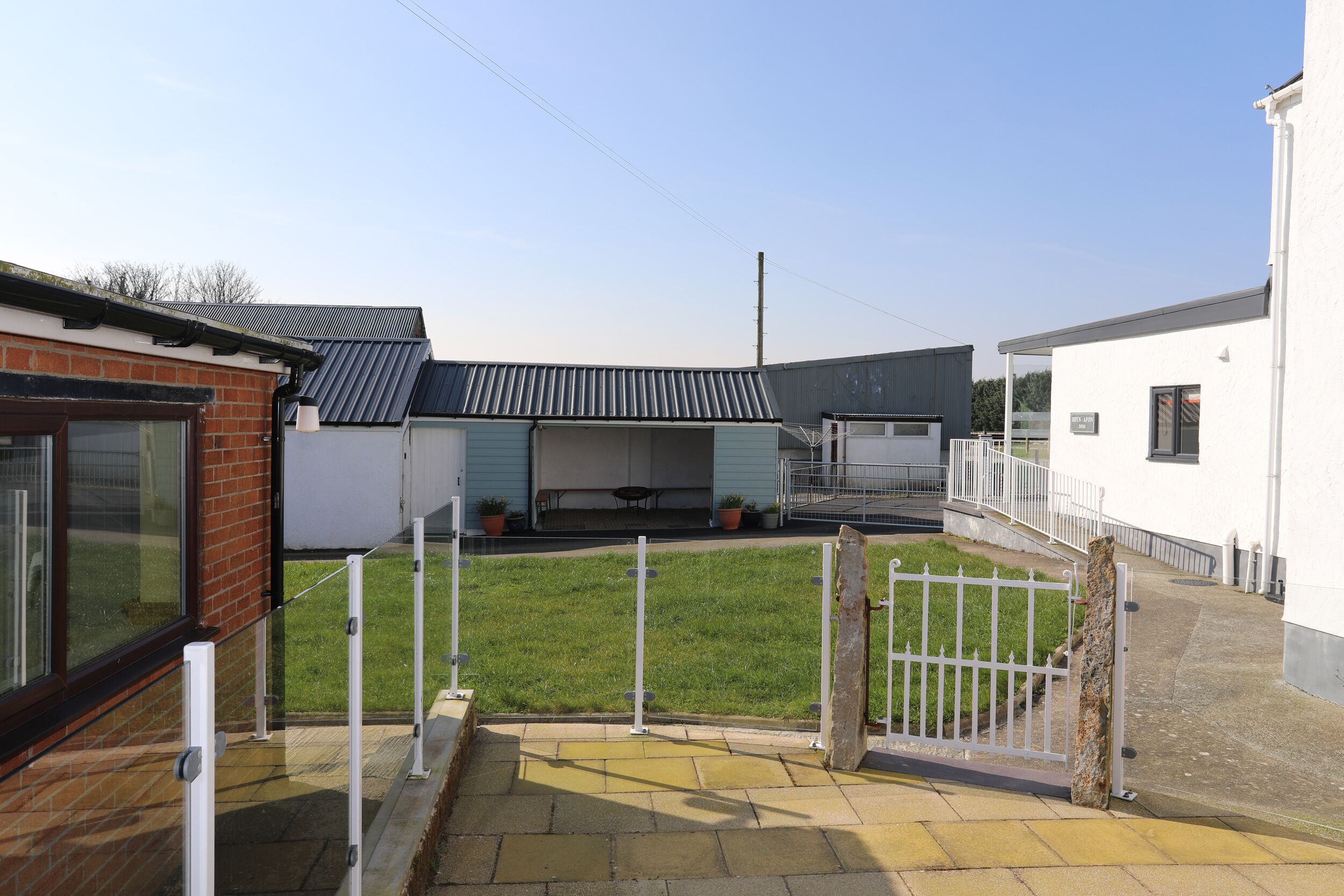 A courtyard with a grassy area, a white fence, and a brick building with a metal roof.