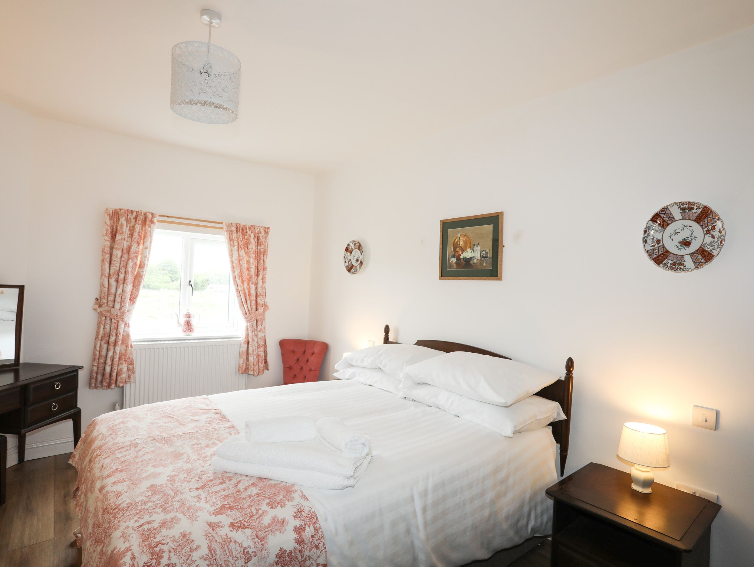 A bedroom with a bed, a nightstand, a window with curtains, a wall-mounted picture, and a ceiling light.