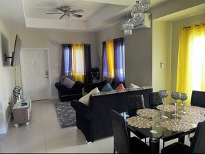 Relax in this stylish living room with a sofa, dining table, and mounted TV.
