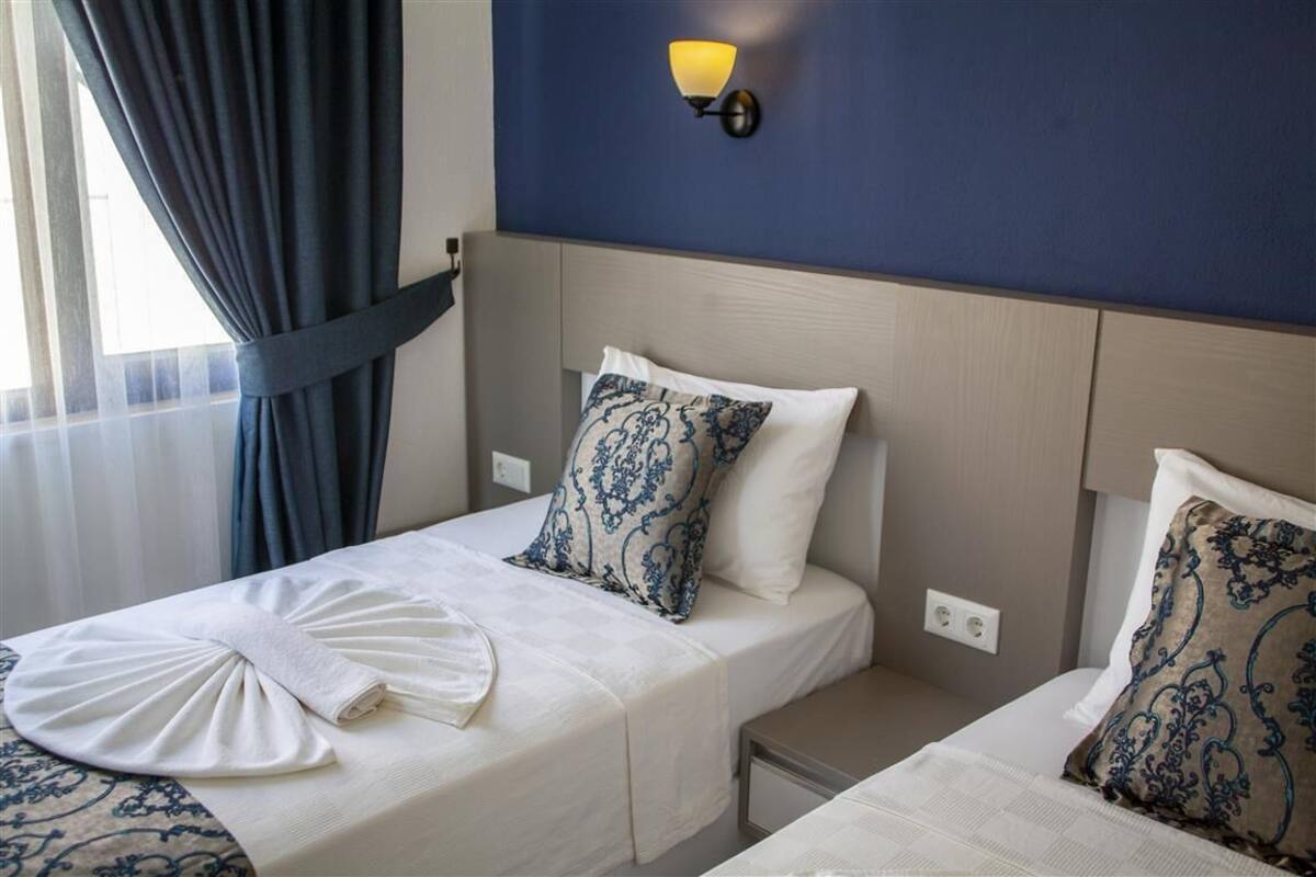 A hotel room with two beds, a wall-mounted light fixture, and a window with curtains.