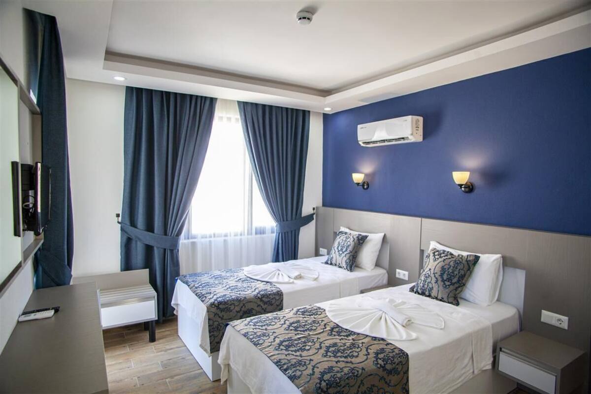 A hotel room with two beds, a desk, a TV, and a window with curtains.