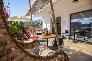 A wicker swing chair with cushions, a table with fruit and drinks, and outdoor seating with umbrellas. - Demyra Boutique Hotel (Demre)