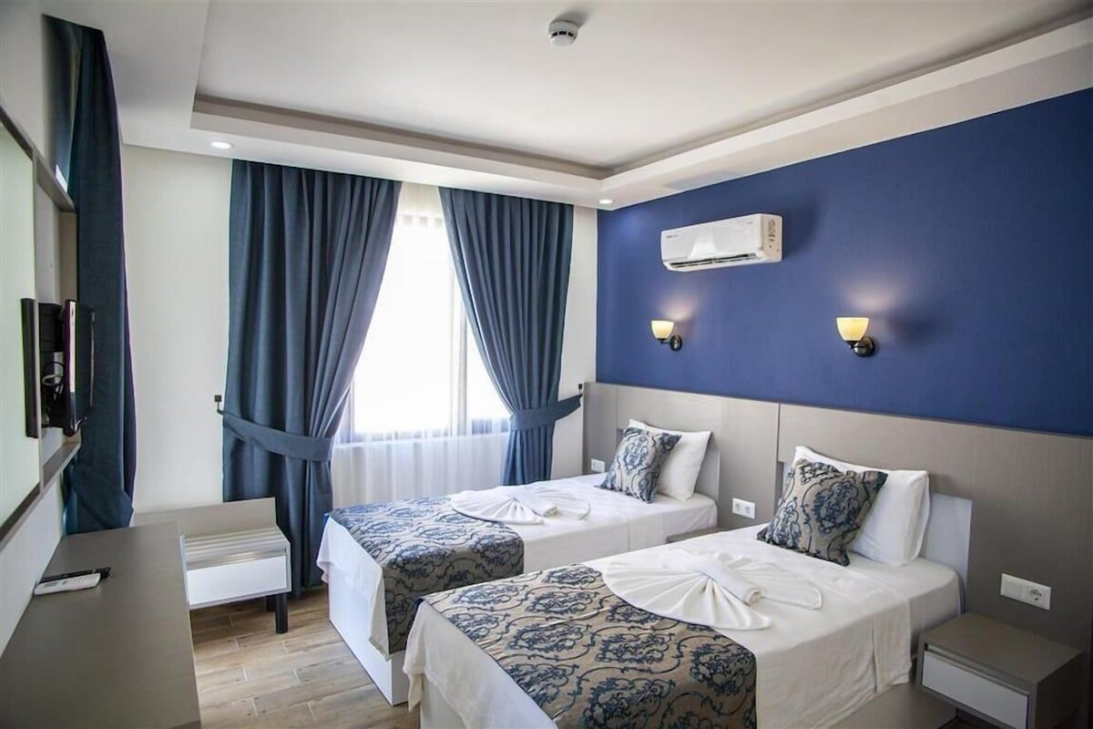 A hotel room with two beds, a desk, a chair, a TV, and an air conditioning unit.