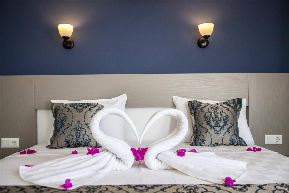 A hotel room with a bed, two wall-mounted lights, and decorative pillows.