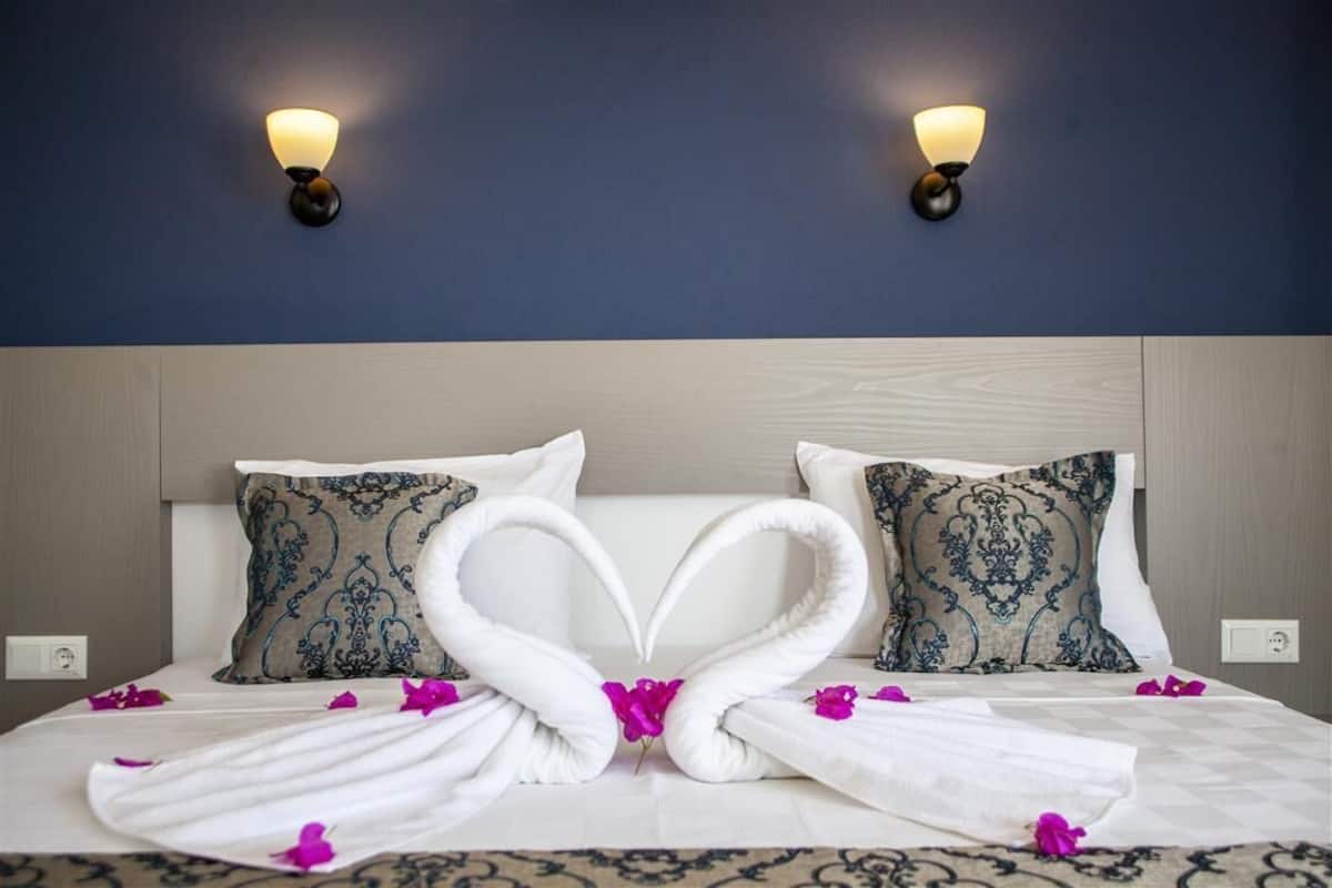 A hotel room with a bed, two wall-mounted lights, and decorative pillows.