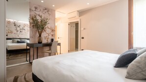 Ein modernes Hotelzimmer mit einem großen Bett, einem Schreibtisch mit Stuhl, einer Vase mit Blumen und einem Spiegel an der Wand.
