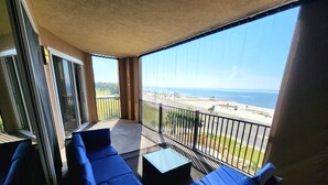 Un balcón con asientos acolchados azules, una mesa de vidrio y vistas a la playa y al océano.