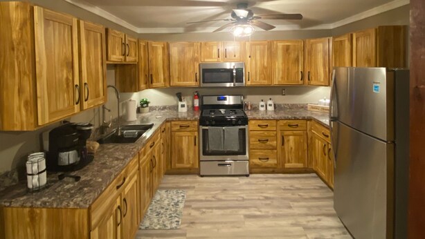 Una cocina con armarios de madera, un refrigerador de acero inoxidable, un microondas, una estufa y un ventilador de techo.