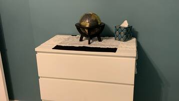 A white dresser with drawers, a globe on top, and a framed picture on the wall.