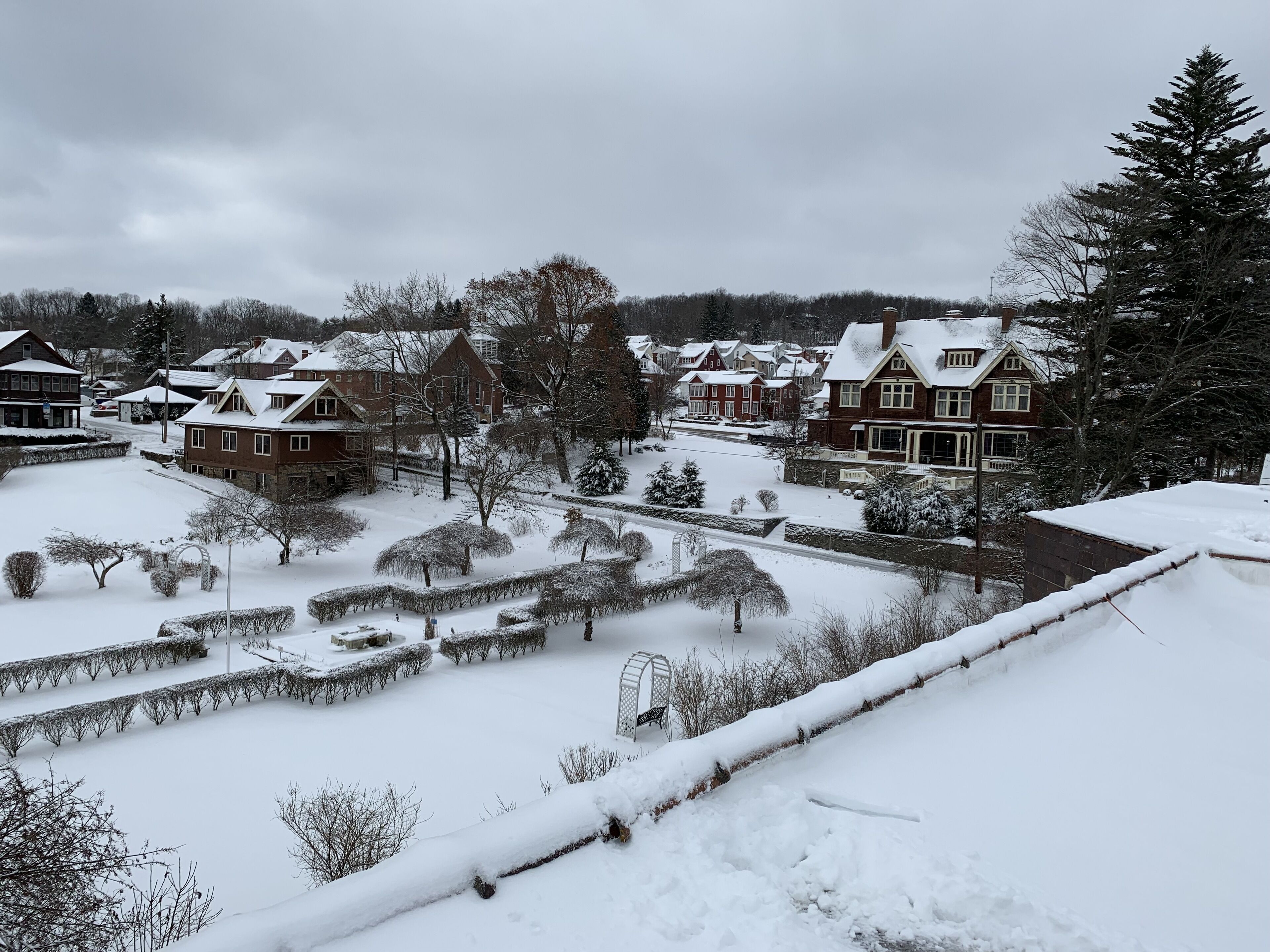 A snow-covered residential area with houses, a clear sky, and a well-maintained garden.