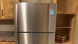 Un refrigerador de acero inoxidable en una cocina con armarios de madera y un reloj en la pared.