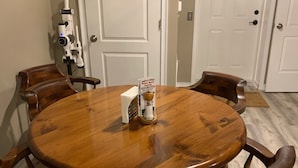 Una mesa de madera redonda con seis sillas, una puerta blanca y una pared blanca al fondo.