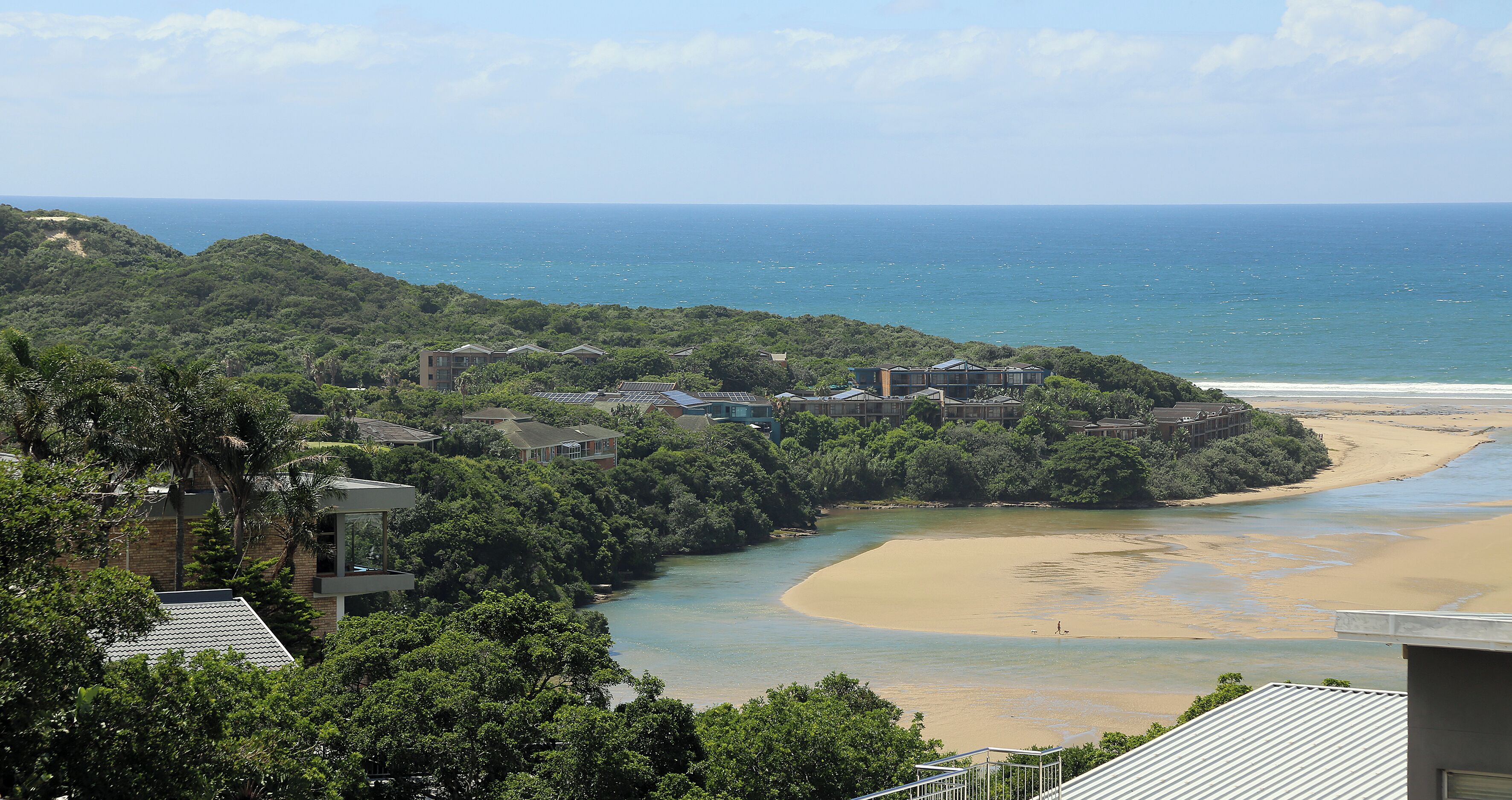 A coastal property with a beach, dense greenery, and a view of the ocean.
