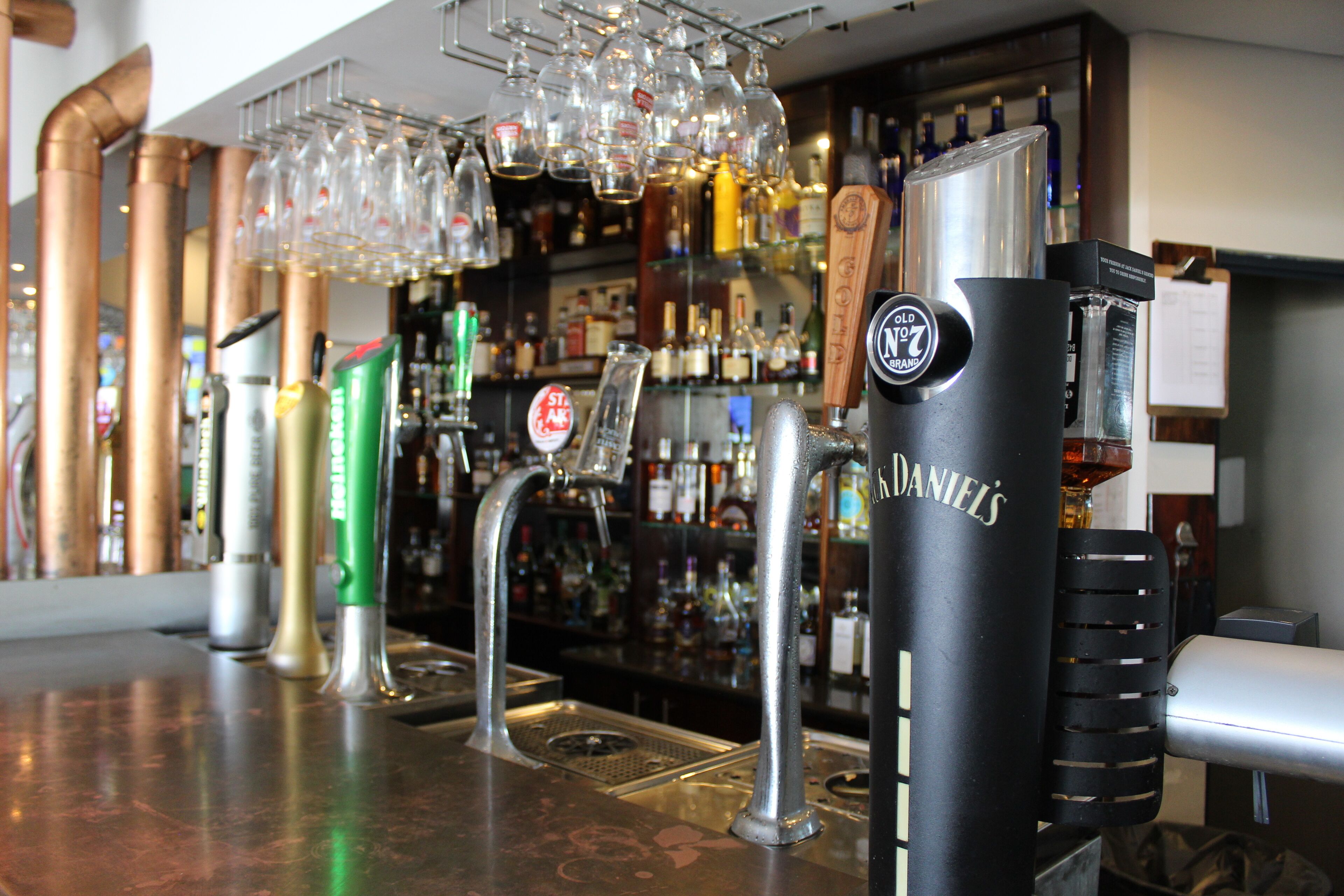 Una zona de bar con una grifo etiquetado "NOLD'S" y una variedad de botellas y vasos en estantes.