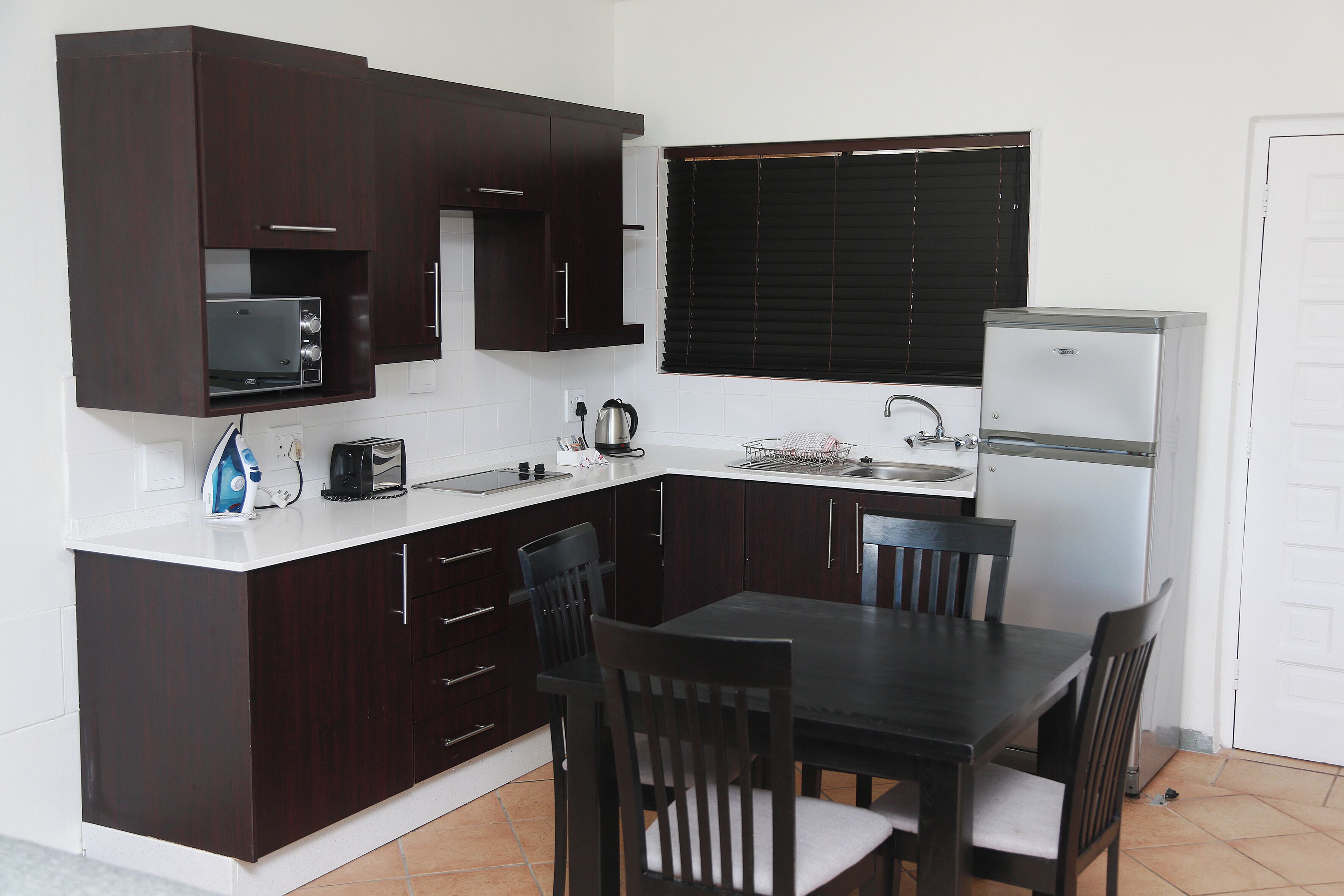 A compact kitchen with dark wooden cabinets, a microwave, a kettle, a toaster, and a refrigerator.
