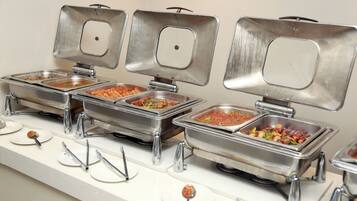 A buffet setup with multiple stainless steel chafing dishes containing various foods, each with a ladle and spoon for serving.