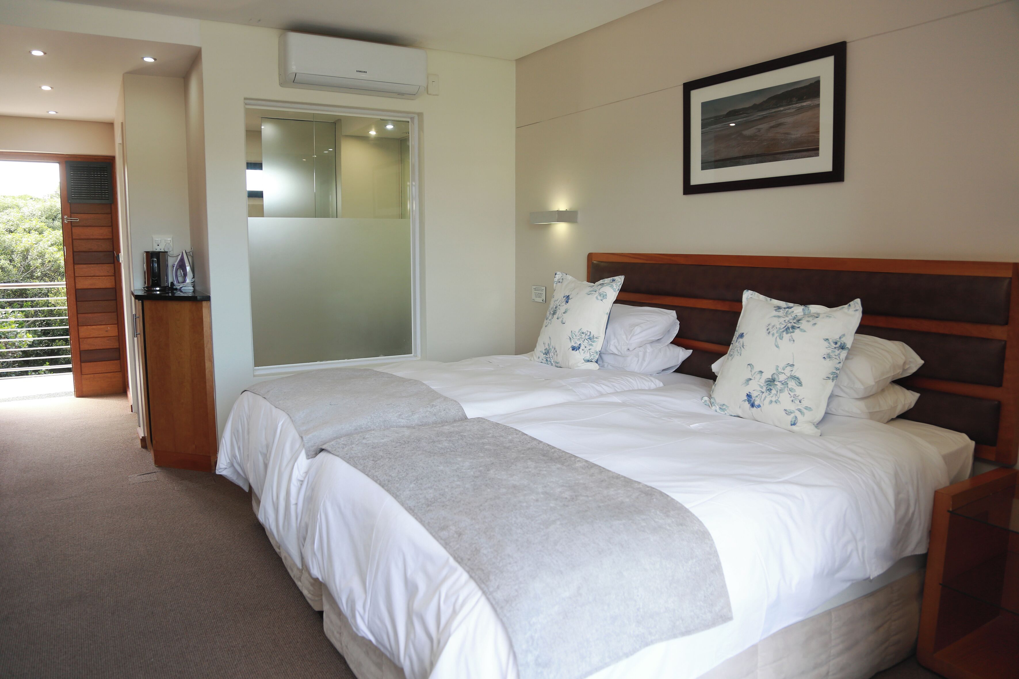 A bedroom with a large bed, a wooden headboard, a bedside table, a nightstand, and a framed picture on the wall.