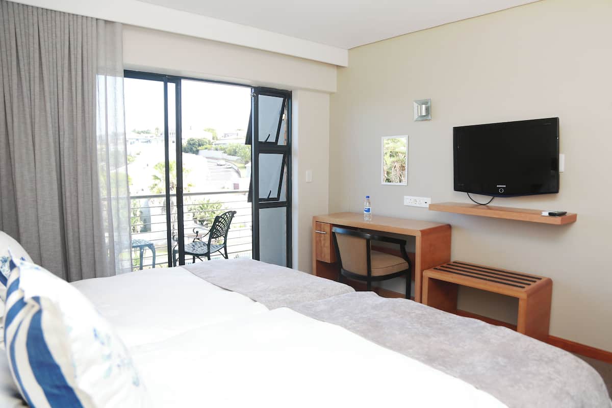 A hotel room with a bed, a desk, a chair, a television, and a balcony with a view of the outside.
