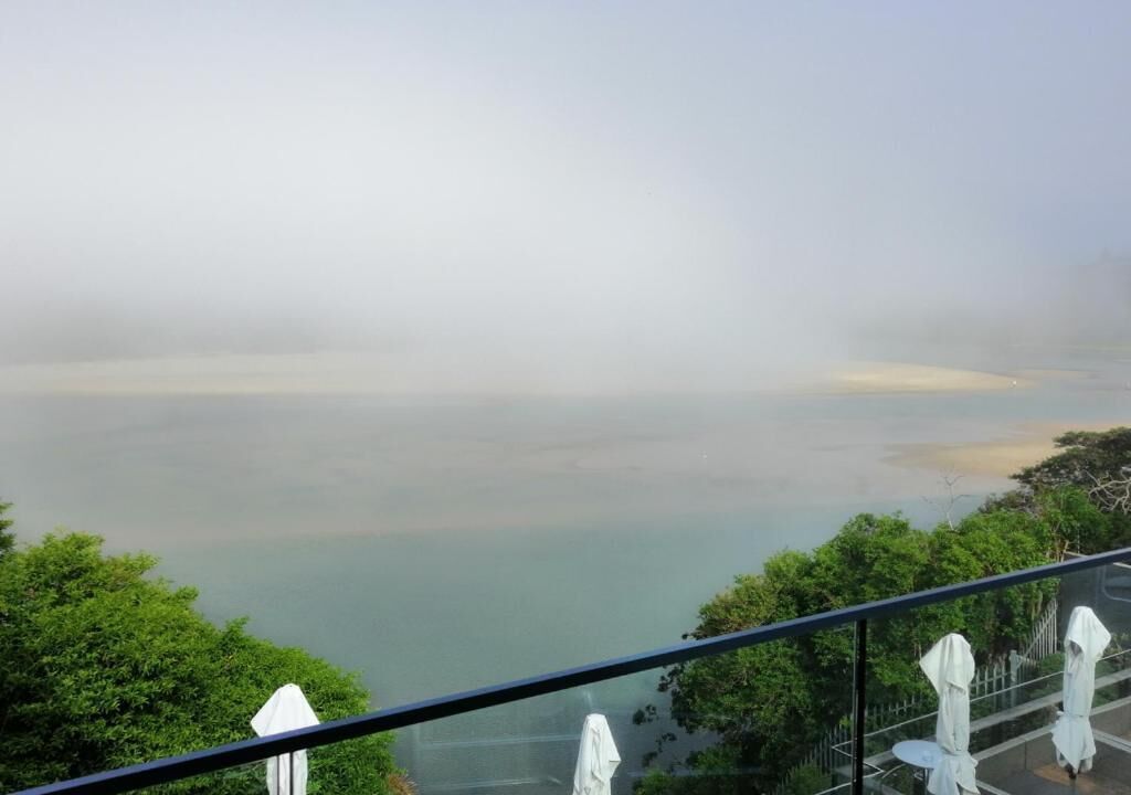 A view from a balcony overlooking a calm body of water, with trees and a clear sky.
