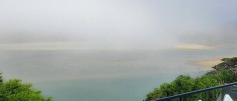 A view from a balcony overlooking a calm body of water, with trees and a clear sky.
