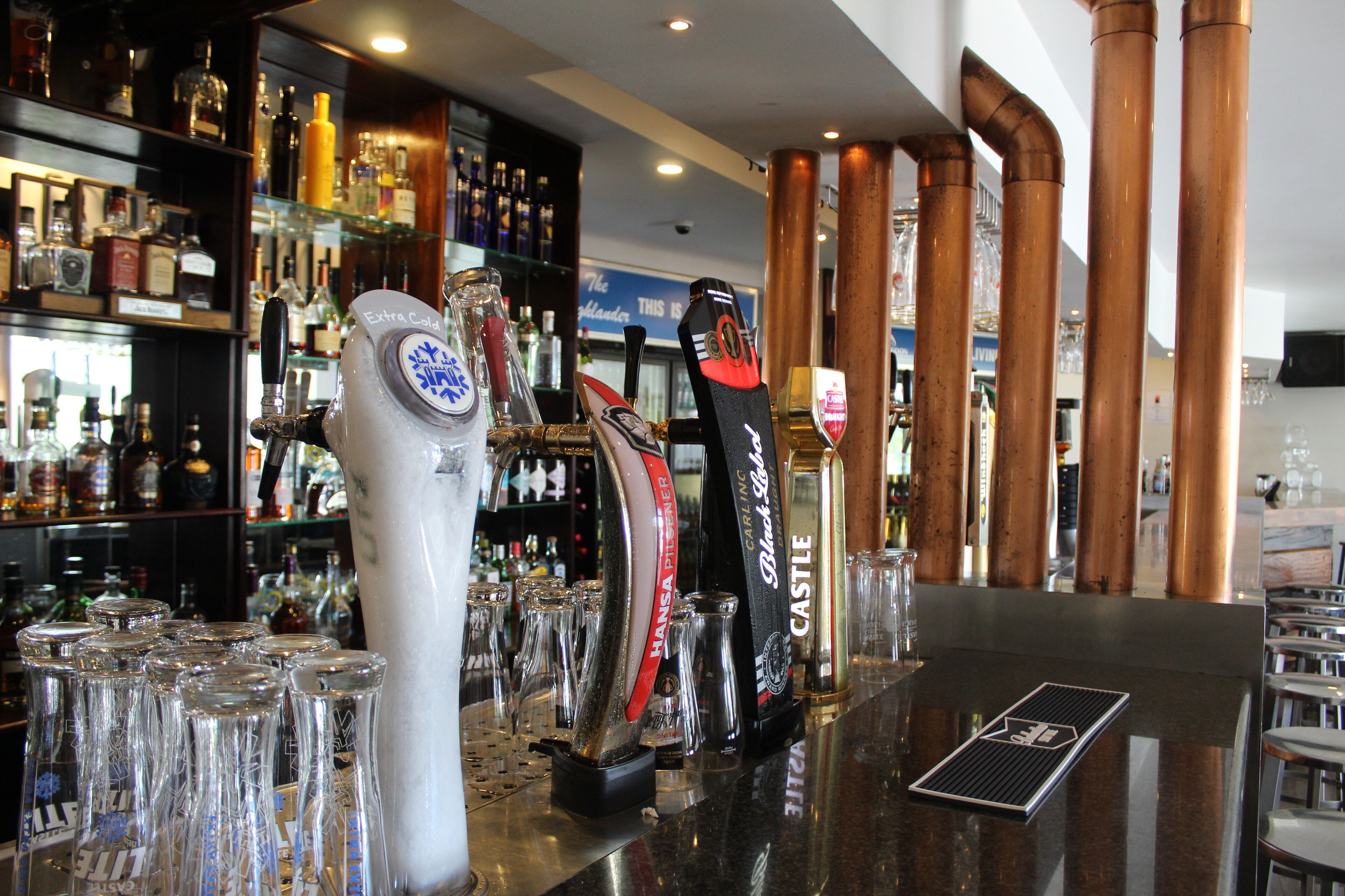 A bar area with multiple taps and glasses, shelves with bottles, and a polished counter.