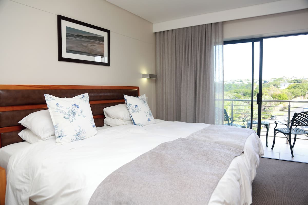 A hotel room with a large bed, a framed picture on the wall, and a balcony with outdoor furniture.